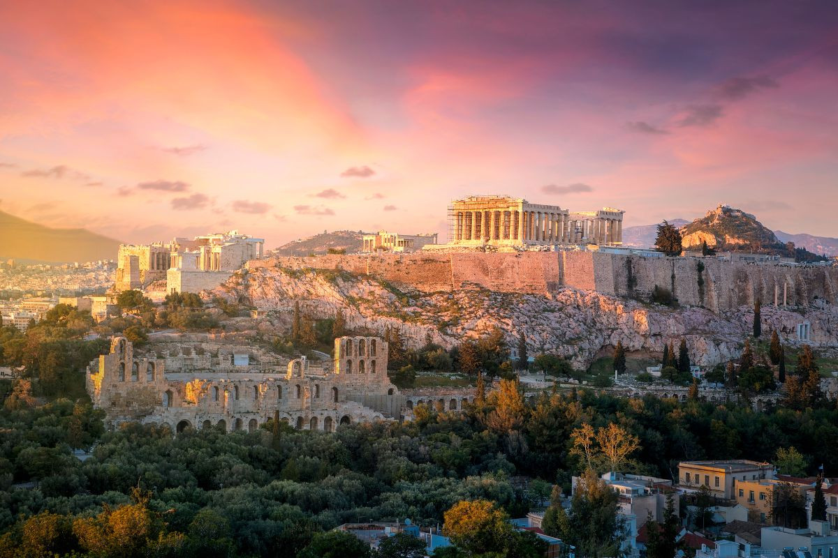 Sunset view of the Acropolis in Athens, with the Parthenon and surrounding ruins visible.